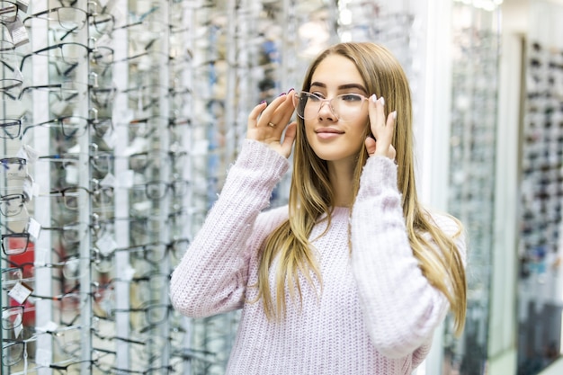 Lächelndes blondes Mädchen im weißen Pullover wählen neue medizinische Brille im professionellen Geschäft