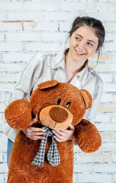 Lächelndes entzückendes Mädchen, das Teddybär hält und zur Seite schaut Foto in hoher Qualität