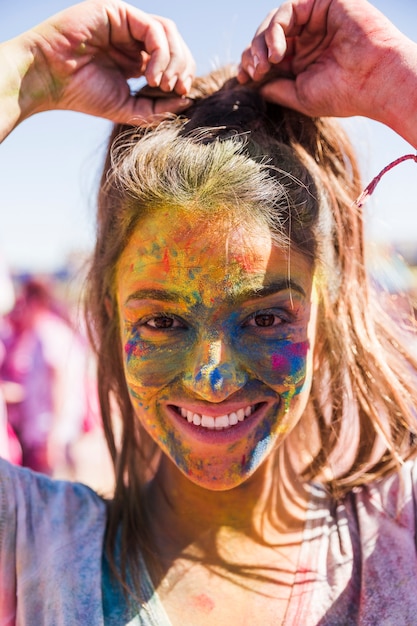 Lächelndes Gesicht der jungen Frau bedeckt mit der holi Farbe, die Kamera betrachtet