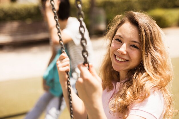 Lächelndes glückliches Schulmädchen, das auf Schwingen sitzt