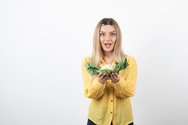 lächelndes hübsches Frauenmodell, das Blumenkohl steht und hält.