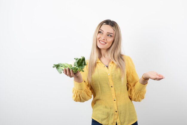 lächelndes hübsches Frauenmodell, das Blumenkohl steht und hält.