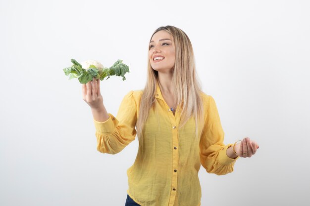 lächelndes hübsches Frauenmodell, das Blumenkohl steht und hält.