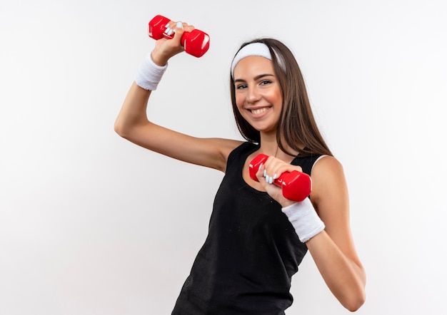 Lächelndes hübsches sportliches Mädchen, das Stirnband und Armband trägt Hanteln, die auf weißem Raum lokalisiert werden