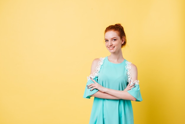 Lächelndes ingwermädchen im kleid, das mit verschränkten armen aufwirft und schaut