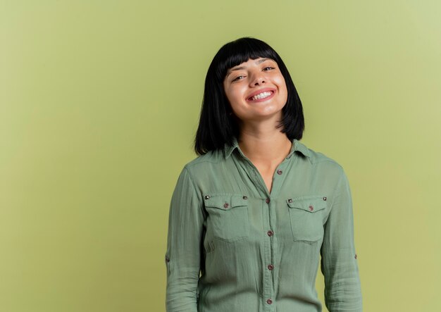 Lächelndes junges brünettes kaukasisches Mädchen betrachtet Kamera lokalisiert auf olivgrünem Hintergrund mit Kopienraum