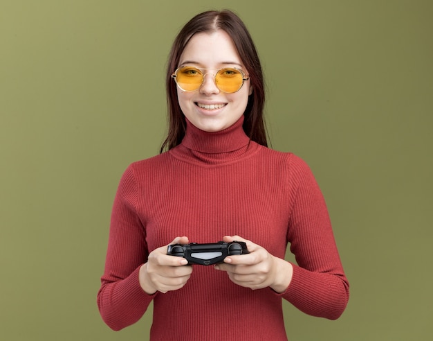 Lächelndes junges hübsches Mädchen mit Sonnenbrille, das einen Gamecontroller-Joystick beim Spielen hält