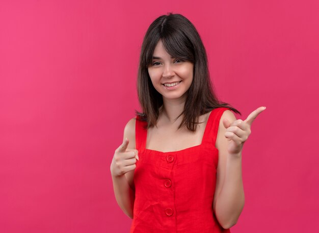 Lächelndes junges kaukasisches Mädchen zeigt zur Seite mit beiden Händen auf lokalisiertem rosa Hintergrund mit Kopienraum