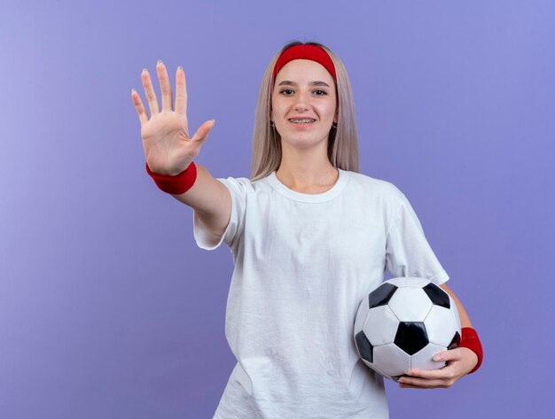 Lächelndes junges kaukasisches sportliches Mädchen mit Zahnspangen, die Stirnband tragen