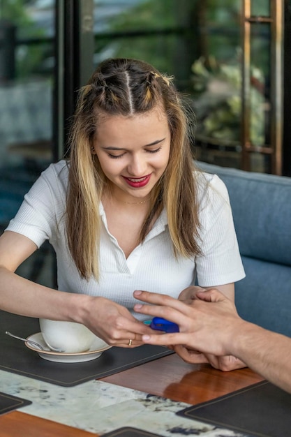 Lächelndes junges Mädchen, das im Restaurant sitzt und auf ihr Telefon schaut