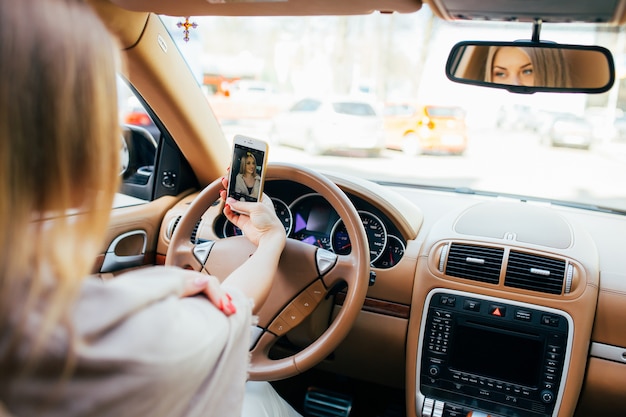 Lächelndes junges Mädchen, das Selfie-Bild mit Smartphone-Kamera im Freien im Auto macht