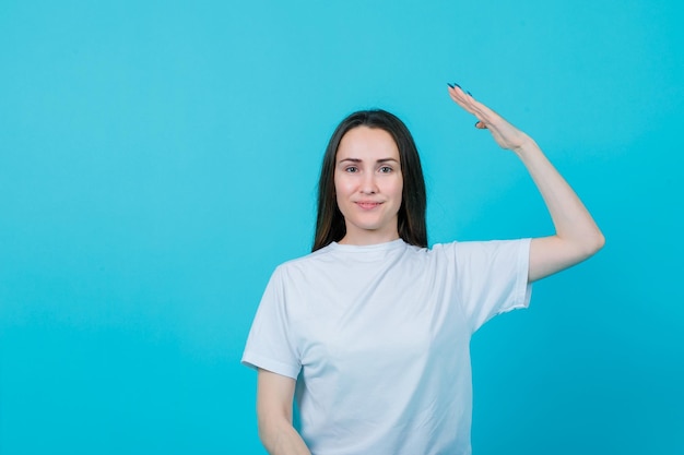 Lächelndes junges Mädchen hebt ihre Hand auf blauem Hintergrund