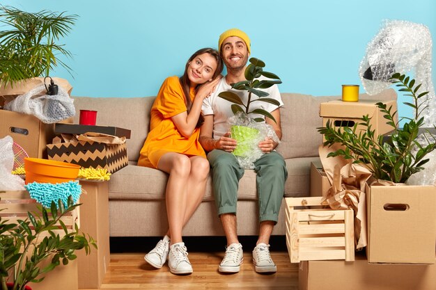 Lächelndes junges Paar, das auf der Couch sitzt, umgeben von Kisten