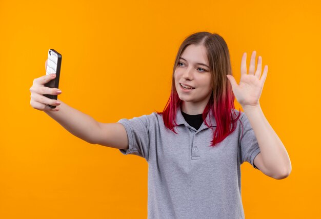 Lächelndes junges schönes Mädchen, das graues T-Shirt trägt, das selfie auf lokalisiertem gelbem Hintergrund nimmt