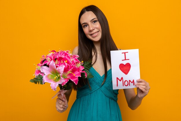 Lächelndes kippendes schönes junges Mädchen mit Blumenstrauß und Grußkarte zum Muttertag