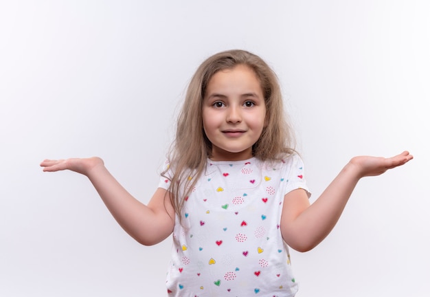 Kostenloses Foto lächelndes kleines schulmädchen, das weißes t-shirt trägt, das zeigt, welche geste auf lokalisiertem weißem hintergrund