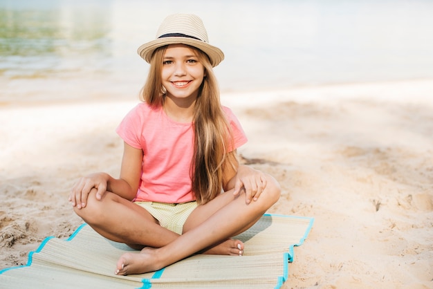 Lächelndes Mädchen, das am Strand sitzt