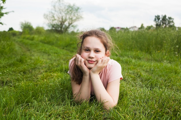 Lächelndes Mädchen, das auf Gras liegt und Kamera im Park betrachtet