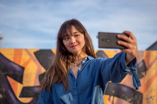 Lächelndes Mädchen, das ein Selfie an einem Skatepark unter dem Sonnenlicht und einem bewölkten Himmel nimmt