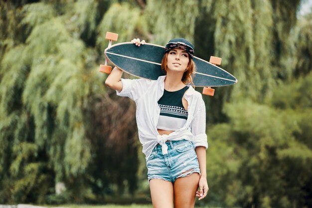 Lächelndes Mädchen, das Haltung nahes Porträt zeigt, Longboard haltend