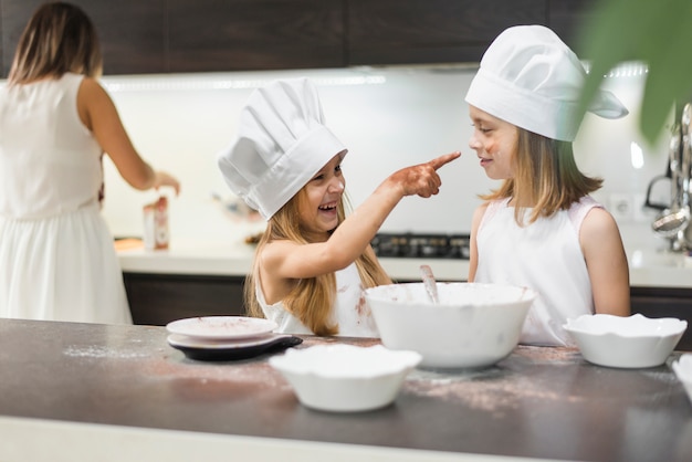 Lächelndes Mädchen, das ihre Schwester mit den unordentlichen Händen in der Küche zeigt