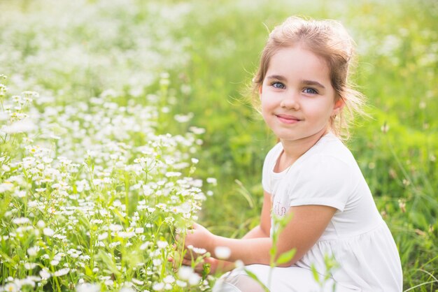 Lächelndes Mädchen, das nahe dem Wildflower auf dem Gebiet sich duckt