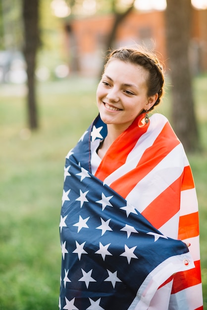 Lächelndes Mädchen eingewickelt in der amerikanischen Flagge in der Natur