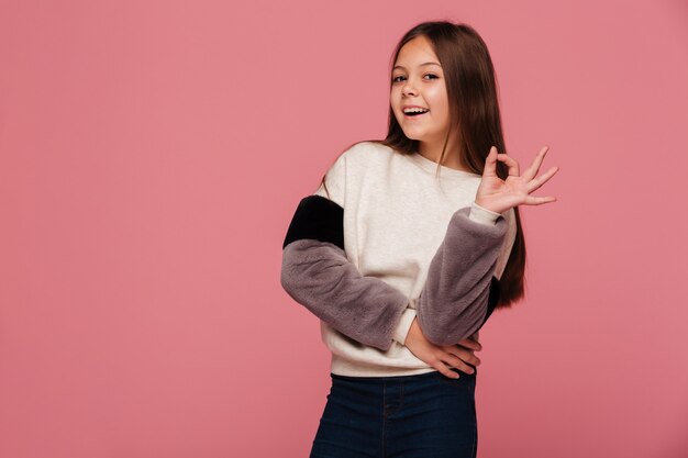 Lächelndes Mädchen in der Strickjacke, die okaygeste schaut und zeigt