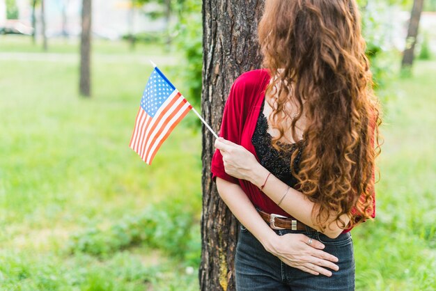 Lächelndes Mädchen mit amerikanischer Flagge vor Baum