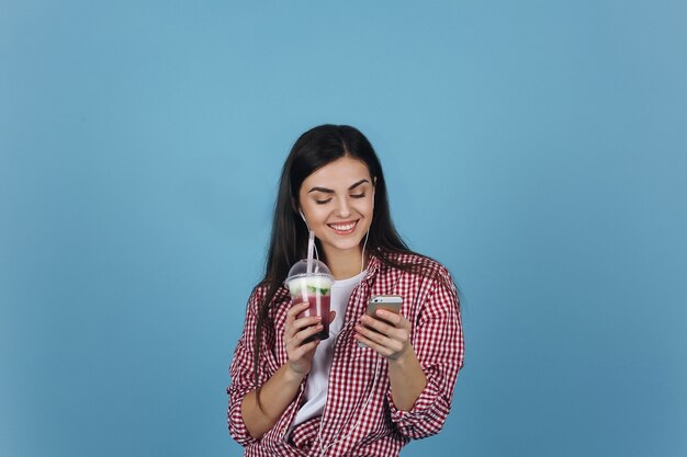 Lächelndes Mädchen mit einem Milchshaken überprüft ihren Smartphone