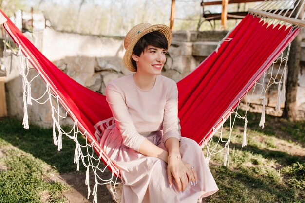 Lächelndes Mädchen mit eleganter Maniküre, die langes Retro-Kleid trägt, das draußen im sonnigen Tag ruht