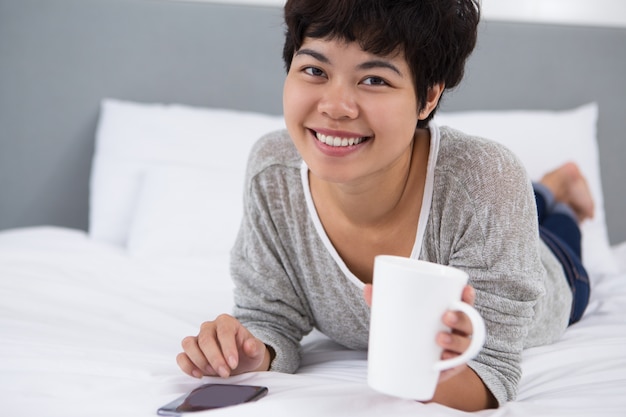 Lächelndes Mädchen mit Smartphone und Tee trinken