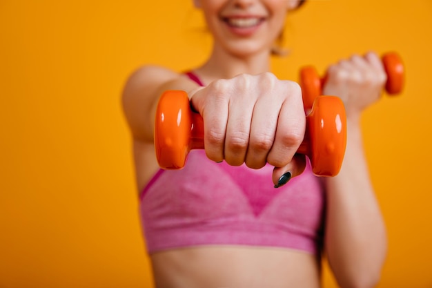 Lächelndes Mädchen posiert mit Hanteln Sportliche junge Frau beim Training auf gelbem Hintergrund