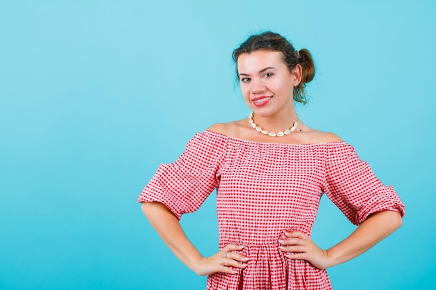 Kostenloses Foto lächelndes mädchen schaut in die kamera, indem es die hände auf die taille auf blauem hintergrund legt