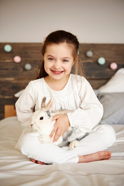 Lächelndes Mädchen umarmt ihr Kaninchen im Bett