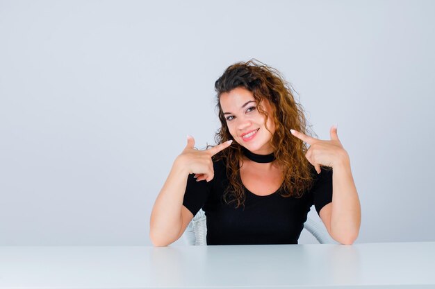 Lächelndes Mädchen zeigt ihr Lächeln mit Zeigefinger auf weißem Hintergrund