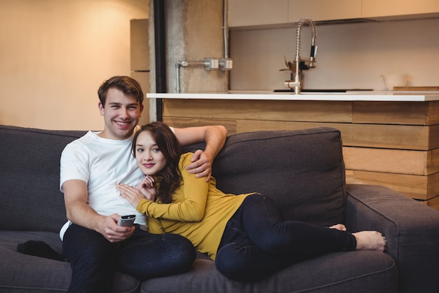 Lächelndes Paar, das auf einem Sofa sitzt und im Wohnzimmer fernsieht