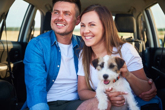 Lächelndes Paar und ihr Hund sitzen im Kofferraum