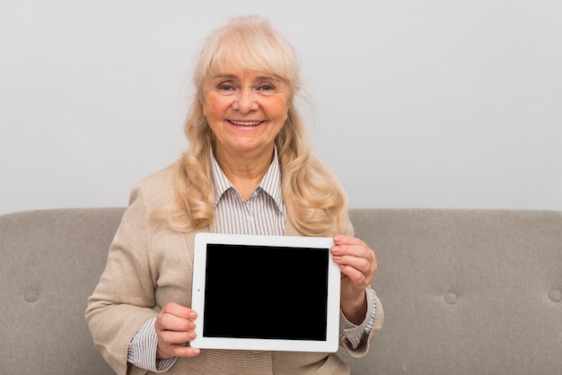Lächelndes Porträt der blonden älteren Frau, die digitale Tablette mit leerem Bildschirm zeigt
