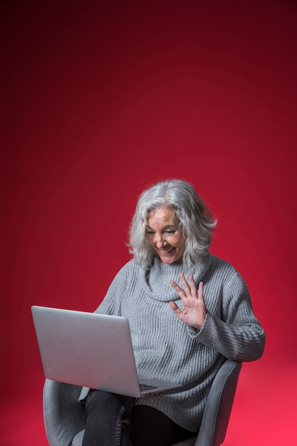 Kostenloses Foto lächelndes porträt einer älteren frau, die ihre hand während video plaudernd auf laptop wellenartig bewegt