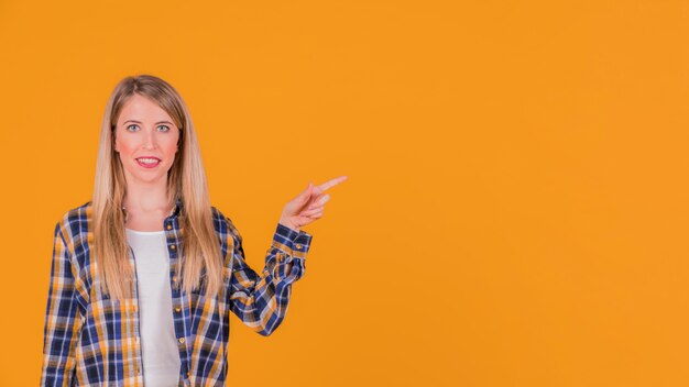Lächelndes Porträt einer jungen Frau, die ihren Finger auf etwas auf orange Hintergrund zeigt