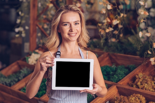 Lächelndes Porträt eines blonden jungen weiblichen Floristen, der leere digitale Tablette zeigt