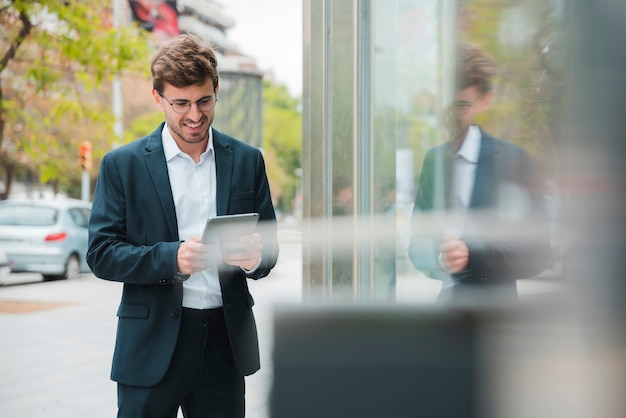 Lächelndes Porträt eines jungen Geschäftsmannes unter Verwendung der digitalen Tablette an draußen