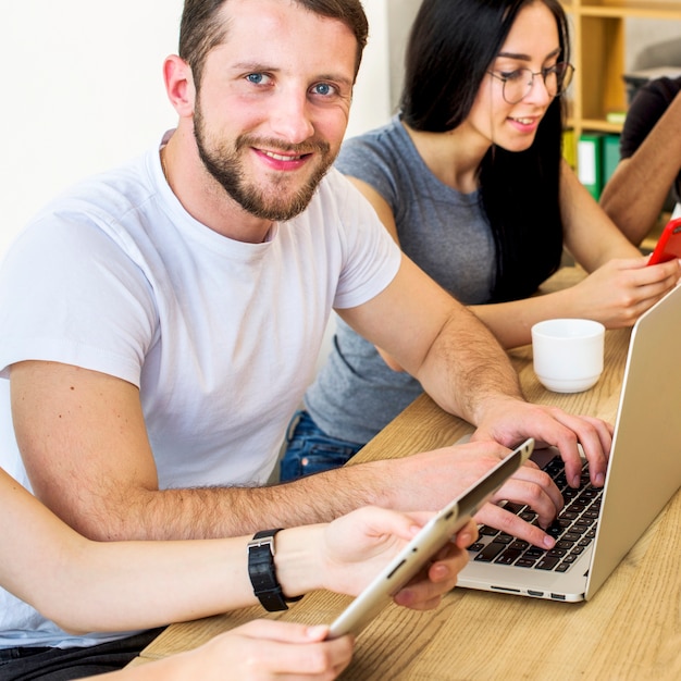 Lächelndes porträt eines jungen mannes, der an laptop über hölzernem schreibtisch arbeitet