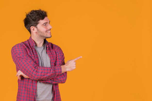 Lächelndes Porträt eines jungen Mannes, der seinen Finger gegen einen orange Hintergrund zeigt