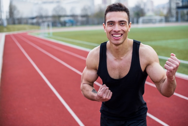 Lächelndes porträt eines männlichen athleten, der seine faust zusammenpreßt, nachdem rennen gewonnen worden ist