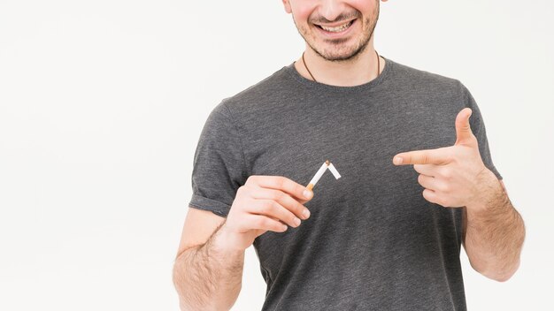 Lächelndes Porträt eines Mannes, der die gebrochene Zigarette lokalisiert auf weißem Hintergrund zeigt