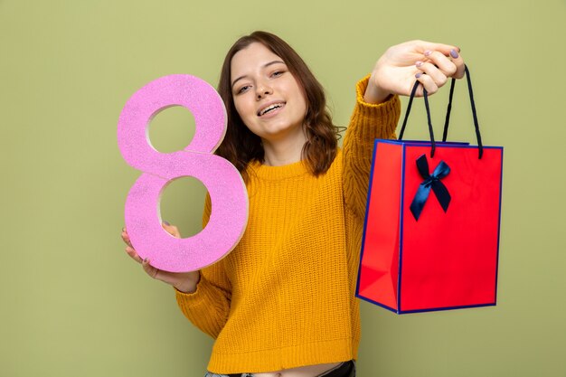 Lächelndes schönes junges Mädchen am glücklichen Frauentag, der Nummer acht mit Geschenktüte hält
