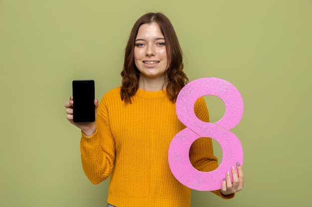 Lächelndes schönes junges Mädchen am glücklichen Frauentag, der Nummer acht mit Telefon hält