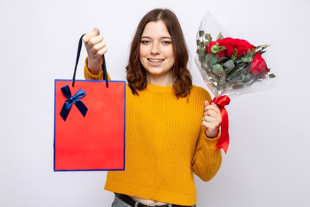 Lächelndes schönes junges Mädchen, das Geschenktüte mit Blumenstrauß hält